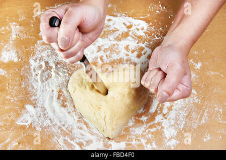 Donna nervoso trafigge il cuore dell'impasto con un coltello da cucina Foto Stock