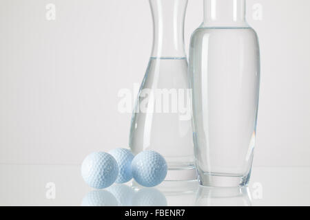 Due vasi con acqua pulita e palline da golf su un tavolo di vetro Foto Stock