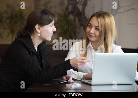 Sorridente due giovani donne caucasici sulla riunione, discutere di affari, lavorando insieme a fianco di laptop Foto Stock