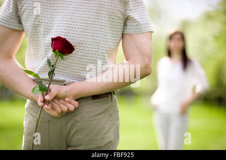 Coppia di amanti su un data focus sul giovane uomo di ritorno che è in possesso di una rosa rossa mentre si guarda la sua ragazza avvicinando Foto Stock