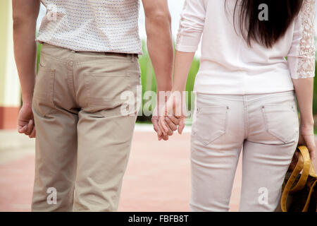 Matura in amore, attraente giovane uomo e donna sulla data di romantiche passeggiate, tenendo le mani sulla strada, vicino delle gambe, schiena vie Foto Stock