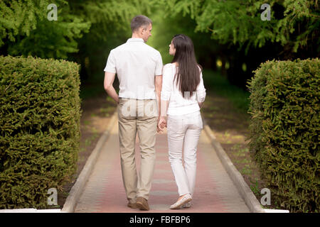 Matura in ama camminare nel parco Holding Hands, attraente giovane uomo e donna su data, guardando ogni altro, parlando, full lengt Foto Stock