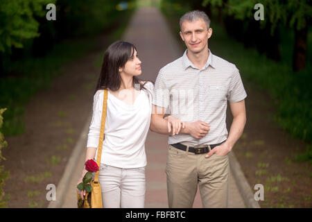 Ritratto di giovane in ama camminare insieme su una data d'estate il parco marciapiede, giovane donna con giallo borsetta guardando il suo ragazzo Foto Stock