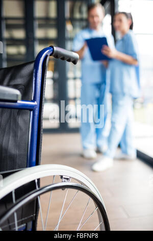 Il personale infermiere portando una sedia a rotelle Foto Stock