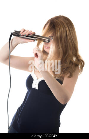 Giovane bella donna bionda la raddrizzatura di suoi lunghi capelli utilizzando ferro elettrico raddrizzatore, studio isolare shot su bianco backgroun Foto Stock