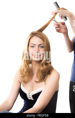 Ritratto di giovane sorridente attraente donna bionda seduta al salone di bellezza con i suoi lunghi capelli tagliati, studio shot, isolato sulla Pentecoste Foto Stock