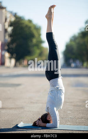 Lo Yoga nella città: bella giovane sportivo da donna che lavorano fuori della strada sulla giornata estiva, facendo supportato headstand postura, salamba Foto Stock