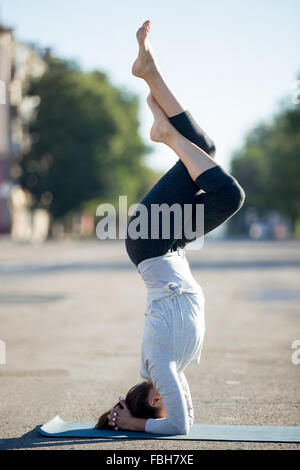 Lo Yoga nella città: bella giovane sportivo da donna che lavorano fuori sulla strada a giornata estiva, facendo Garuda Salamba Sirshasana, variati Foto Stock