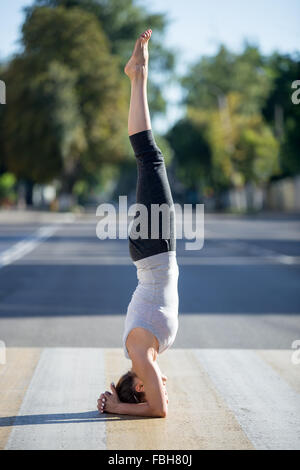 Lo Yoga nella città: bella giovane sportivo da donna che indossa abbigliamento sportivo lavoro su crosswalk pedonale sulla strada vuota sulla stree Foto Stock