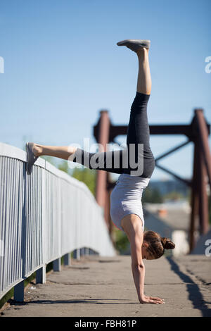 Lo Yoga nella città: sportivo bella ragazza adolescente che lavora fuori sul vecchio ponte sul giorno di estate, appoggiata sulla ringhiera, facendo variazione Foto Stock