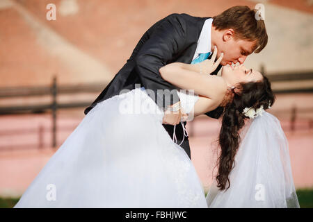 Lo sposo dolce Sposa inclinato, tenendo tra le braccia e la bacia appassionatamente, matrimonio foto in una giornata di sole, di sfondo le pareti color sabbia. Sposi dancing a park street tango. Foto Stock