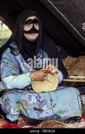 Oman. Donna con Burqa rendendo cesto per il cammello latte. Foto Stock