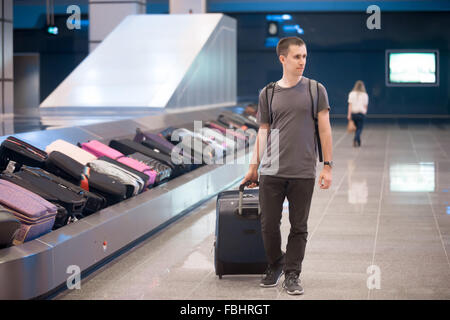 Giovane uomo bello passeggero in suo 20s a piedi nella sala degli arrivi del terminal aeroportuale edificio dopo la raccolta dei suoi bagagli presso Foto Stock