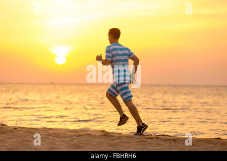 Uno stile di vita sano: bel giovane uomo che lavora fuori all'aperto, corre veloce sulla sabbia a riva al tramonto o l'alba, vista posteriore Foto Stock