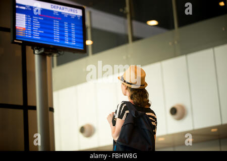 Giovane donna in 20s nel cappello di paglia e abiti estivi con carry-in, il bagaglio a mano nello zaino in attesa del volo in aeroporto moderno termi Foto Stock