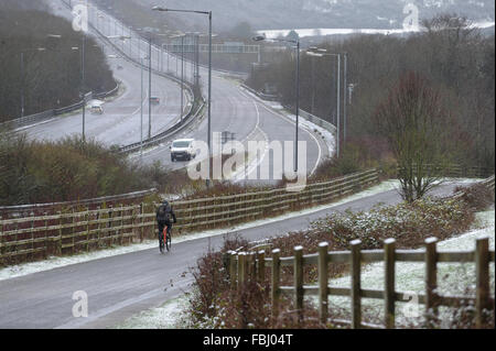 Un ciclista scorre verso il basso con cautela una strada ghiacciata accanto alla A27 e coperta di neve le colline e la campagna a nord di Brighton in East Sussex, Inghilterra. Foto Stock