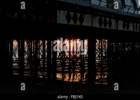 Sunrise dietro South Parade pier a Southsea. Sunburst risplende attraverso la formazione di ruggine pontili. Bagliore dorato con riflessione nel mare. Foto Stock