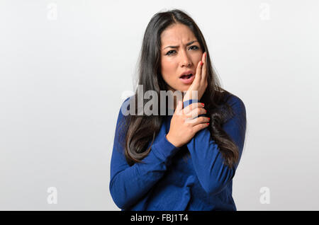 Giovane donna con un mal di denti di aggancio sulla sua guancia con la mano mentre accigliata nel dolore, corpo superiore su bianco Foto Stock