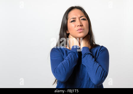 Attraente giovane donna con un mal di gola stringendo il suo collo con la mano e un grimace del dolore come lei tenta di inghiottire Foto Stock