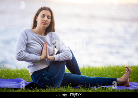 Bella giovane sportivo da donna che lavorano fuori sulla strada sul tappeto blu, facendo esercizi di allungamento riverbank nel parco, seduta a metà Foto Stock