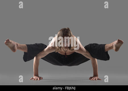 Sporty giovane uomo in pantaloni neri facendo rafforzare lo Yoga asana in piedi in equilibrio del braccio, una variazione della postura di lucciola, asana Titt Foto Stock
