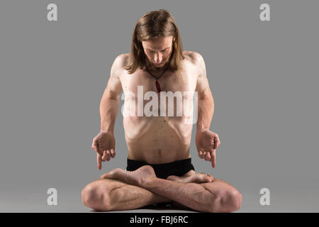 Sporty muscolare yogi giovane uomo seduto a gambe incrociate in lotus postura, meditando, praticare Pranayama tecniche in padmasana, Foto Stock