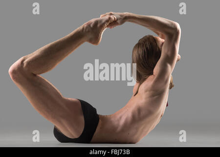 Sporty muscolare yogi giovane uomo facendo esercizio backbend, dhanurasana, prua postura, studio shot su sfondo scuro, vista laterale Foto Stock