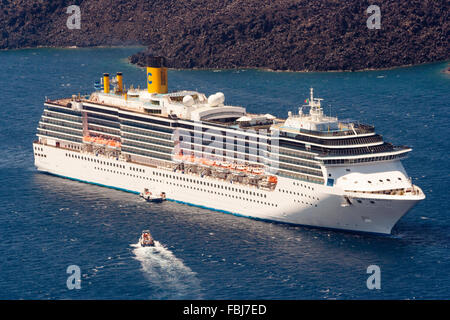 Santorini nel Mare Egeo. Oceaniche lussuosa nave da crociera Costa Mediterranea, visto da sopra, vela su molto mare calmo, una piccola barca ormeggiata sul lato. Foto Stock