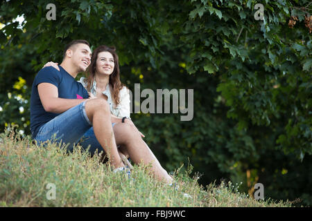 Bella felice coppia giovane in amore indossando abiti casual rilassante sotto acero nel parco, guardando in lontananza, dreami Foto Stock