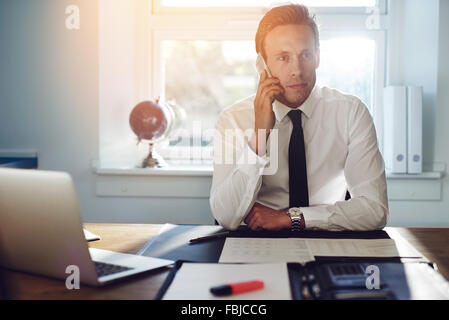 Bianco giovane uomo business parlando al telefono, seduto alla scrivania di indossare tuta e tirante Foto Stock