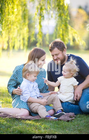 Ritratto di felice bella famiglia di quattro rilassanti sul prato, trascorrere il tempo libero in parco picnic in estate. Giocoso i bambini s Foto Stock