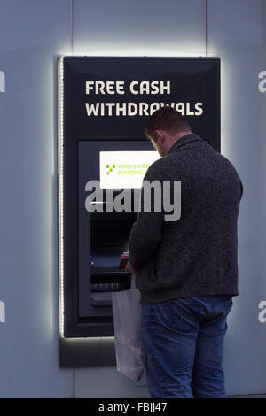 Un uomo utilizza un bancomat ATM offrendo gratuitamente i prelievi di contanti. Foto Stock