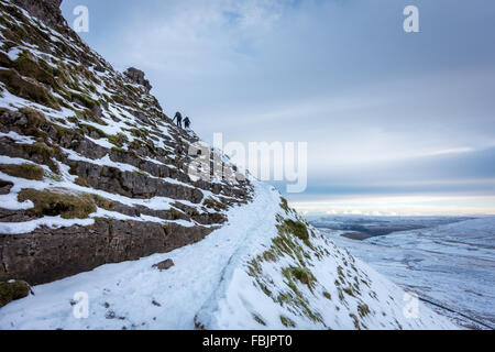 Pen-y-Ghent in inverno con due escursionisti clambering fino al gelido tratto più ripido su un giorno nevoso, Yorkshire Dales. Foto Stock