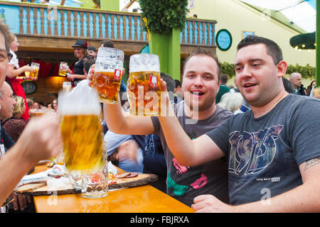 Giovani uomini la tostatura con boccali da birra in una birreria a Oktoberfest a Monaco di Baviera, Germania. Foto Stock