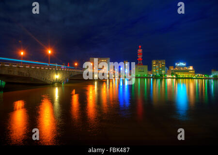 La riflessione di luci dalle costruzioni oltre il fiume nella città di Niigata, Giappone occidentale nuvoloso durante la notte. Foto Stock