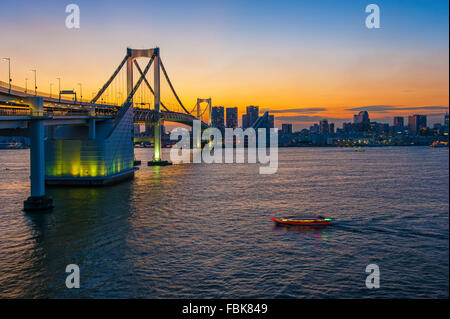 La vista del Ponte di Arcobaleno e il circostante di edifici commerciali da Odaiba isola a Tokyo in Giappone durante il tramonto Foto Stock