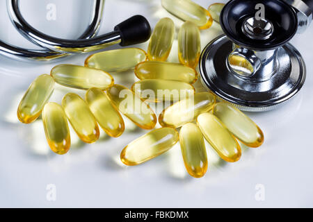 Olio di pesce omega 3 capsule di gel con uno stetoscopio su sfondo bianco con la riflessione. Foto Stock