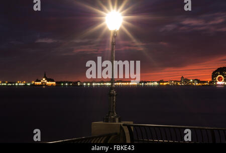 Una lunga esposizione vista di un lampione con il fiume Hudson e Jersey City e Liberty State Park skyline con un tramonto mozzafiato. Foto Stock