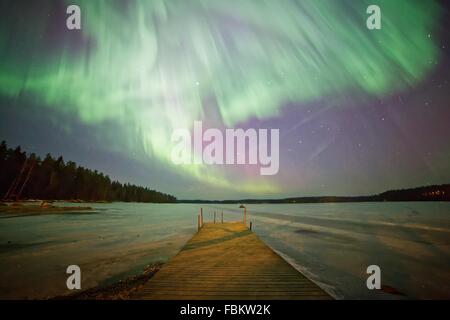 Luci del nord (Aurora Boreale) incandescente nel cielo notturno su un lago ghiacciato in Finlandia. Colori vibranti della corona è chiaramente v Foto Stock