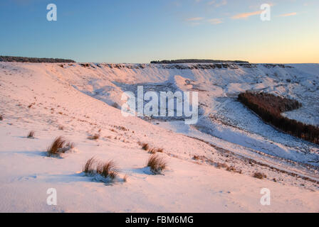 La luminosità del tramonto su un paesaggio innevato al di sopra del villaggio di Charlesworth, Derbyshire in Inghilterra settentrionale. Foto Stock