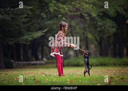 Ragazza che gioca con il suo cucciolo di cane in posizione di parcheggio Foto Stock