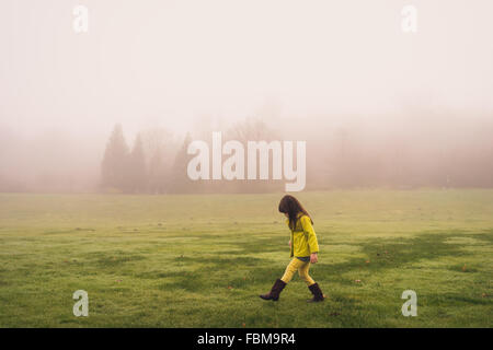 Vista laterale di una ragazza camminare nel parco su un nebbioso giorno Foto Stock