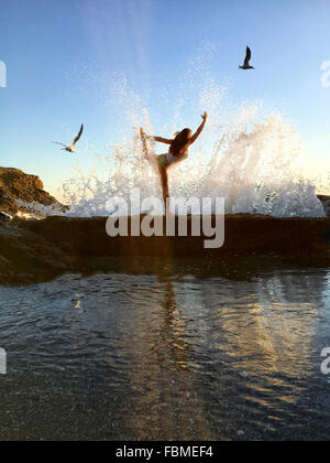 Donna in prua ancora lo yoga pone sulle scogliere a spiaggia Foto Stock