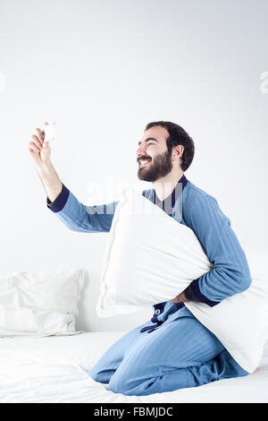 Uomo con il pigiama sul letto prendendo un Selfie con uno smartphone Foto Stock