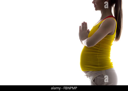 Silhouette di sorridere giovani incinte modello di fitness in sportswear fare yoga, pilates formazione, tenendo le palme in gesto di preghiera Foto Stock