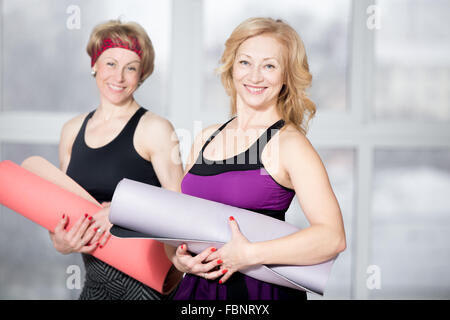 Piscina ritratto di gruppo di due allegro attraente montare le donne anziane in posa di contenimento materassini fitness, lavorando nei club sportivi Foto Stock