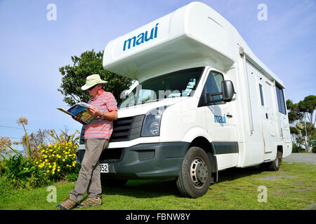 Turista con camper guardando il libro delle mappe sul campeggio a Hawke's Bay, Isola del Nord, Nuova Zelanda Foto Stock