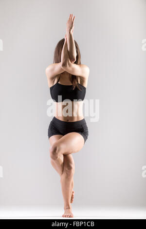 Bella sportiva ragazza Yogi pratiche yoga asana, Garudasana,la posizione dell'Aquila su sfondo grigio, chiave di basso shot Foto Stock