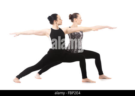 Yogi ragazze facendo asana insieme, fitness training, la pratica dello yoga con il partner, in piedi nella posizione del Guerriero II posa, Virabhadrasana II Foto Stock