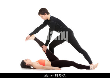 Due sportivi la pratica dello yoga con partner, giovane maschio coach aiutando la ragazza per fare reclinabili a mano alluce pongono, supta Foto Stock